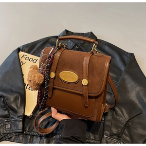 Close-up of retro brown leather satchel with metal logo, bear pendant and woven detail