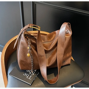 Detail of a brown leather tote bag with gold hardware and braided pendant on a chair