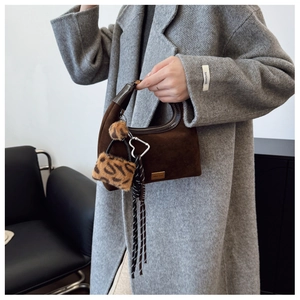 Detail of dark brown suede hobo bag with leopard pouch charm and woven ribbons