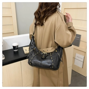 Detail of black leather crescent bag with metal studs and zippers on a model coat