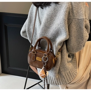 Close-up of brown polished leather crossbody bag with gold plaque and knit charm