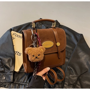 Detail of a brown leather backpack with golden logo plaque and fuzzy bear charm