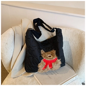 Detail einer gesteppten schwarzen Hobo-Tasche mit Plüschbären-Anhänger und rotem Schal