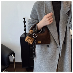 Detail of dark brown suede handbag featuring a heart buckle and leopard faux fur charm