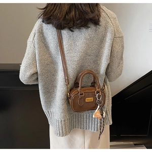 Detail of a brown Boston mini bag featuring a sleek leather finish and woven bag charm