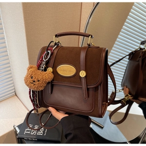 Close-up of vintage brown retro handbag with metallic logo and cute plush bear charm