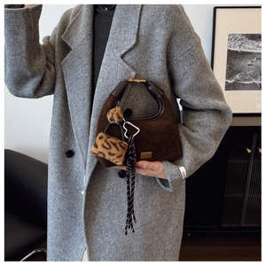 Detail of dark brown suede dumpling bag with leopard pom-pom and striped ribbon