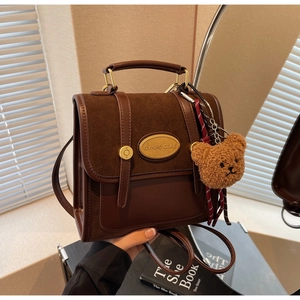 Close-up of retro brown messenger bag featuring suede patchwork and plush bear charm