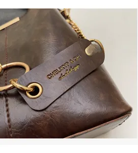 Détail d'un sac à main en cuir marron foncé avec anneaux dorés et étiquette de marque