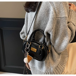 Detail of glossy black leather crossbody bag with golden plaque and baseball charm
