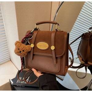 Detail of vintage brown suede satchel with golden hardware and plush bear charm