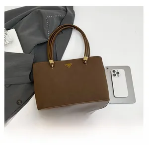 Detail view of brown tote bag with matte leather finish and gold logo next to phone
