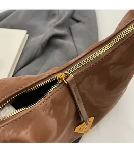 Dettaglio della cerniera dorata e del logo triangolare su una borsa marrone a spalla