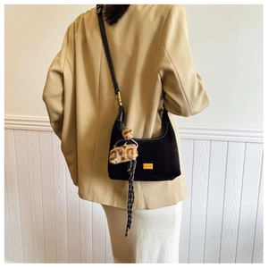 Detail of black suede shoulder bag with leopard pompom and woven strap on model