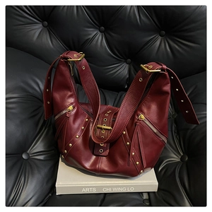 Close-up of burgundy leather bag with gold rivets, tassels, and a buckle on a sofa
