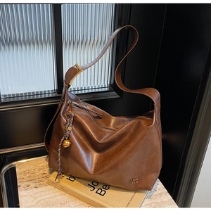 Macro detail of brown leather tote bag with vintage texture and gold bell charm