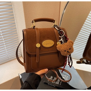 Detail of brown vintage crossbody bag featuring suede textures and a plush bear charm