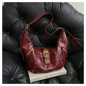 Detailed shot of burgundy leather dumpling bag with gold studs on a black leather sofa