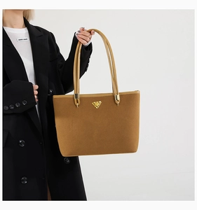 Close-up of a brown suede tote bag with a signature gold triangle plaque detail