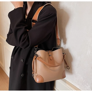 Detail of camel lychee leather bucket bag with wide contrasting shoulder strap on model