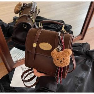 Detail view of brown leather retro crossbody bag featuring a plush bear charm and metal logo
