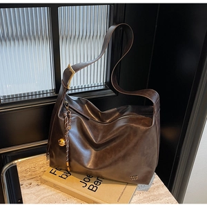 Detail of dark brown leather tote bag showing metal logo and woven bell charm accessory
