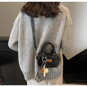 Detail view of black patent leather mini boston bag with baseball charms and gold hardware