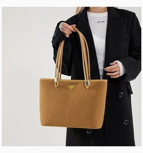 Close-up of caramel suede tote bag featuring a golden triangular metal logo detail