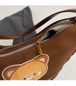 Gros plan sur la fermeture éclair dorée et la broderie ours d'un sac cabas en cuir marron