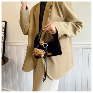 Detail of black suede dumpling bag featuring leopard plush charm and woven rope handle