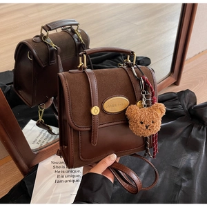 Detail of vintage brown leather satchel featuring gold nameplate and plush bear charm