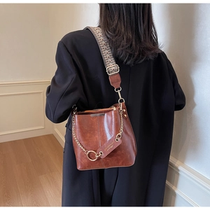 Détail du sac seau marron vintage avec chaîne dorée et bandoulière tissée ethnique