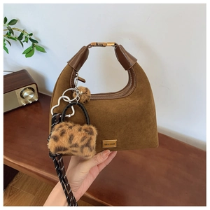 Detail of caramel suede dumpling bag featuring leopard print charm and metal logo