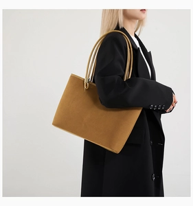 Detail of a large suede tote bag in camel color with cylindrical handles and metal hardware