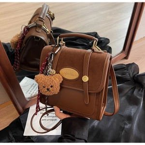 Detail of vintage dark brown crossbody bag with suede texture and gold oval plaque decoration