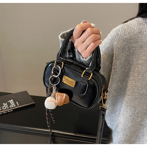 Detail of black glossy patent leather mini Boston bag with baseball glove charm and gold hardware