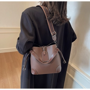 Detail of a brown lychee pattern bucket bag with a wide fabric strap and silver buckle