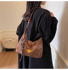 Brown shoulder bag with beaded strap and metallic triangle logo on black blazer