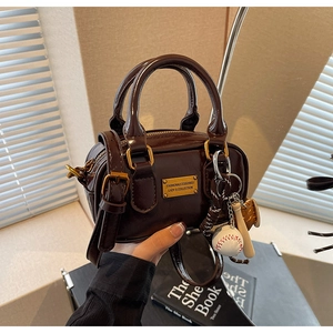 Detail view of mini chocolate patent leather Boston bag with vintage gold logo and baseball charm