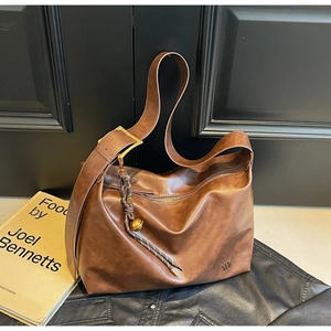 Detail of dark brown leather tote bag with gold buckle and decorative charm on white surface