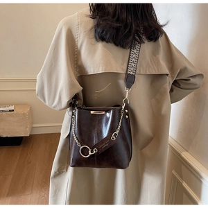 Détail du sac seau en cuir marron avec chaîne dorée et bandoulière tissée