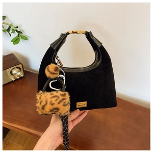 Detail of black suede dumpling bag with gold logo plate and leopard print plush charms