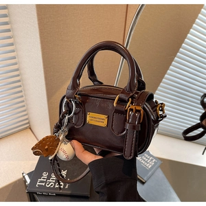 Deep brown retro pillow bag with shiny finish, gold logo plate and creative baseball charm