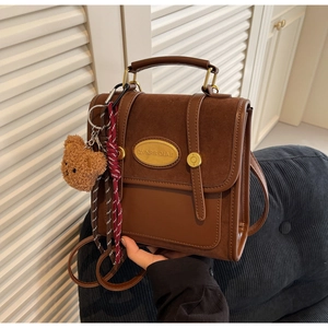 Detail of vintage brown suede crossbody bag featuring a golden logo plate and bear charm