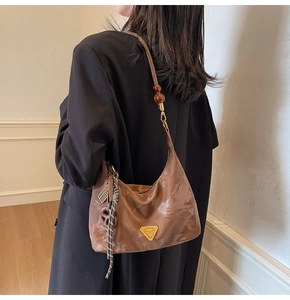 Dettaglio della borsa sottobraccio in pelle marrone con cinturino in ambra e logo oro
