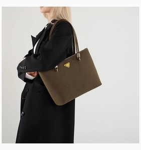 Detail of a large tote bag in dark olive suede with gold triangular logo on black coat