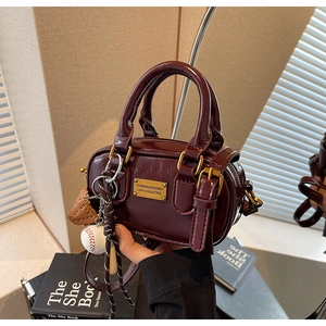 Detail of dark reddish brown faux leather handbag with baseball charm and gold plate