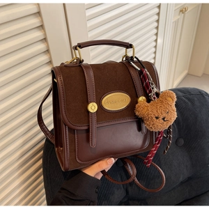 Detail of dark brown vintage satchel showing the metallic logo plate and plush bear charm