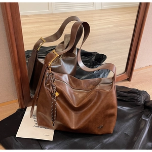 Detailed close-up of brown vintage leather tote with metal buckle and fringe charm