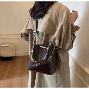 Détail du sac seau marron vintage avec chaîne dorée et large bandoulière à motifs